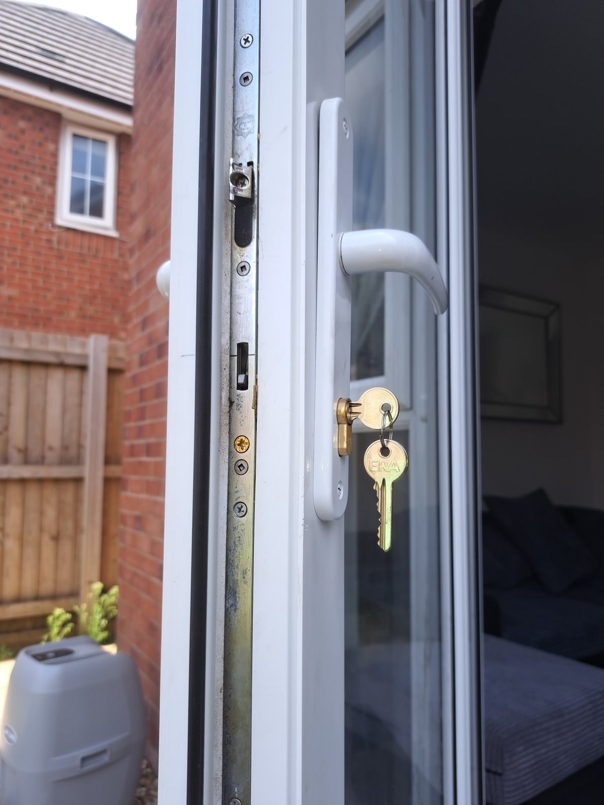 The edge of a white uPVC door showing its multipoint lock, with keys in the new cylinder
