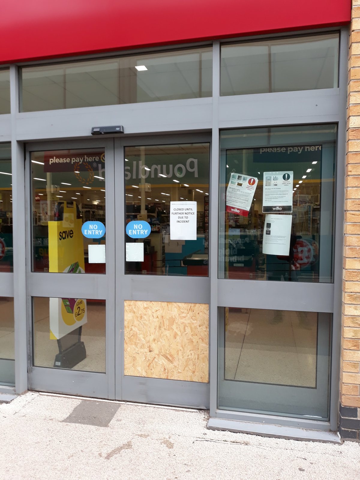 A shop entrance with the damaged lower door panel boarded and secured